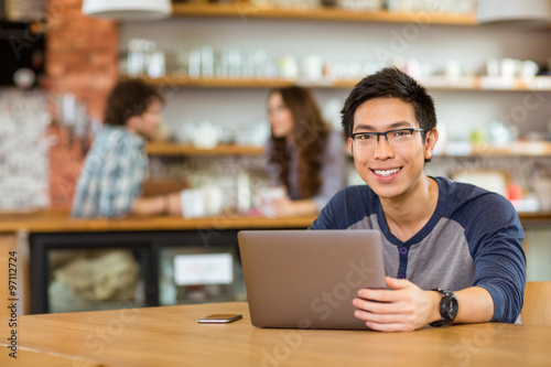 Young cheerful asian man in glasses using laptop