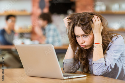 Exhausted stressed young woman with tousled hair using laptop