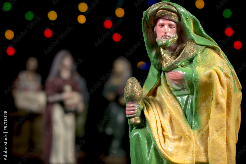 The magi Caspar in front of other Nativity scene figurines and colorful stars at background. Christmas traditions.