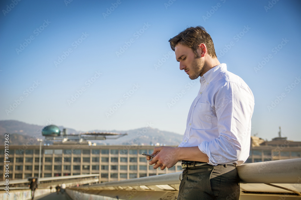 Handsome trendy man using cell phone to type text, outdoor