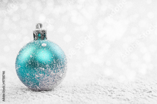 Christmas ball in the snow on blurred light background. A holiday card. Traditional Christmas decorations.