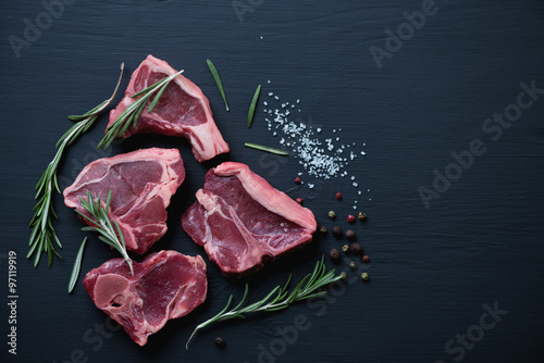 Top view of raw T-bone lamb steaks on a black wooden surface