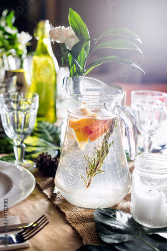 A carafe of fruity beverage with mint and lemon on a decorated table ready for dinner. Beautifully decorated table set for wedding or another event in the restaurant.
