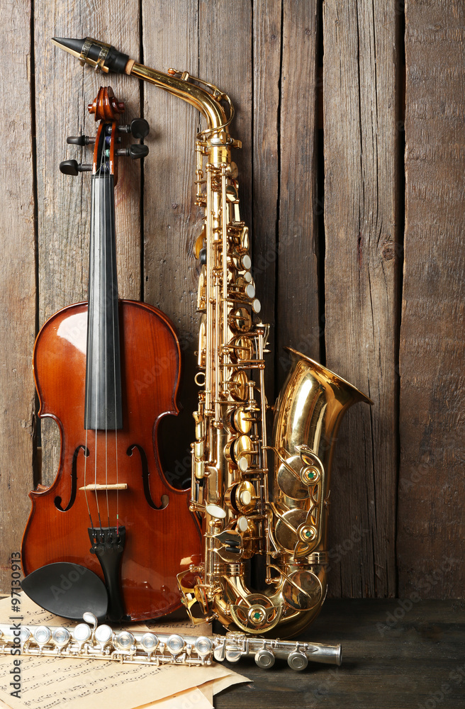 Naklejka premium Musical instruments: saxophone, violin and flute with notes on wooden background