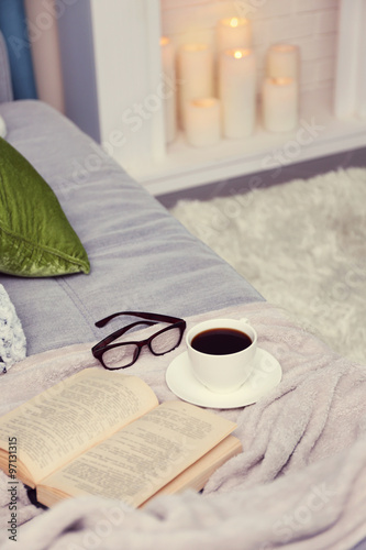 Cup of coffee with book on sofa in room © Africa Studio