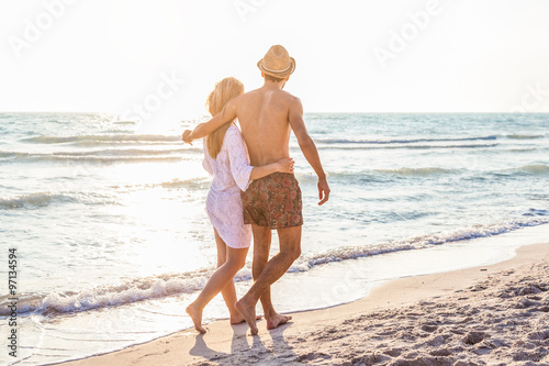 Sunset, sandy beach, a loving couple walks embraced on the deserted beach at sunset during a day at the beach on vacation