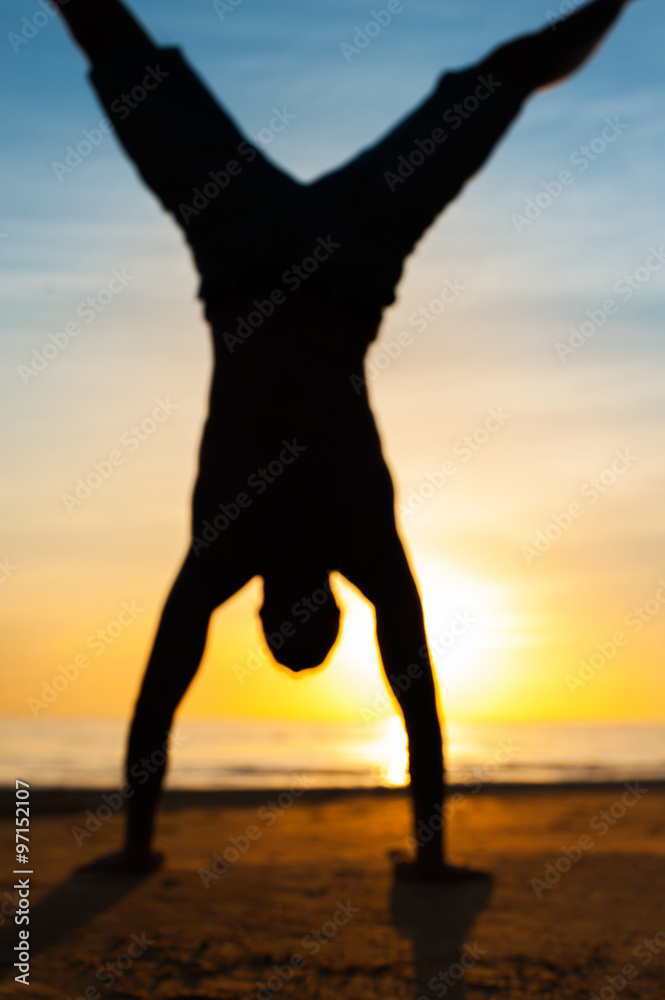Blurred silhouette of young man making handstand on the beach.
