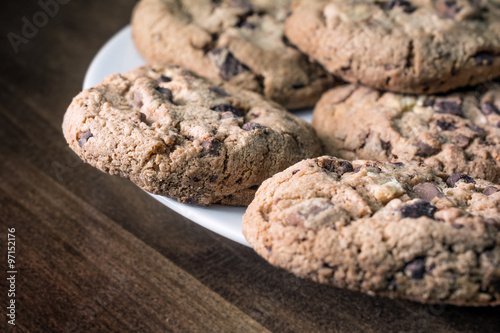 Several Chocolate Cookies Lying On The Edge Of A White Plate On A Wooden Vintage Table photo