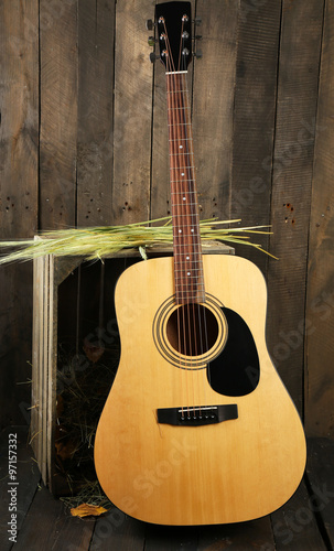 Acoustic guitar against box with hay on wooden background