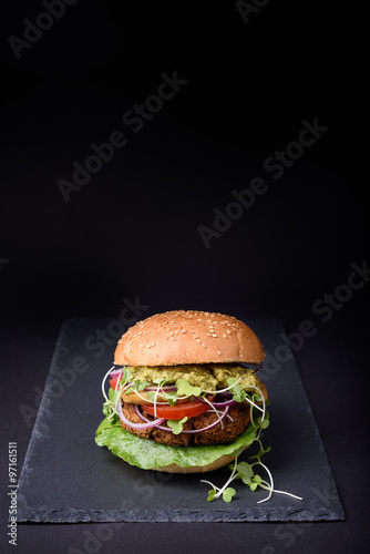 Veggie falafel burger with pesto sauce, tomato, cress salad and onion on black slate board. Space for text.