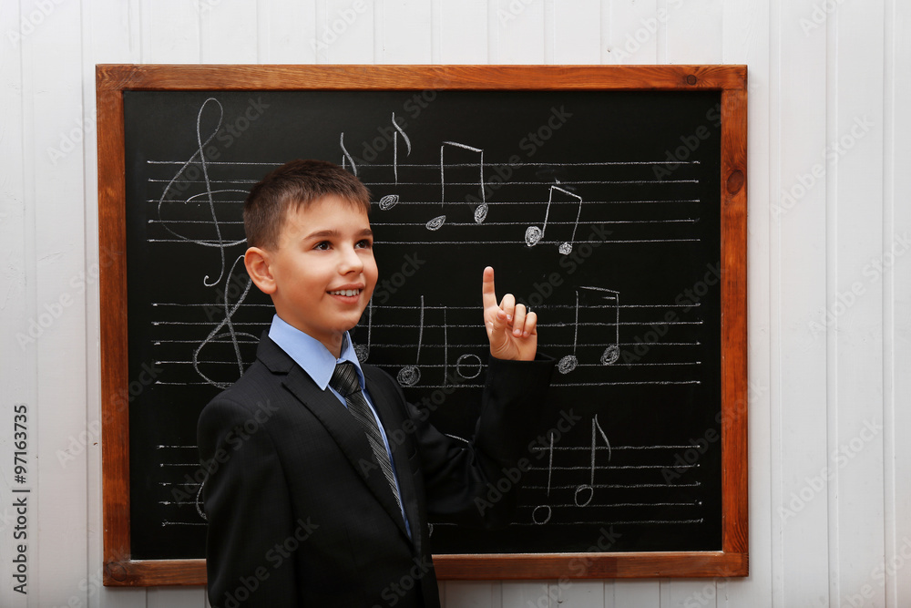 Young cute schoolboy standing at the blackboard with musical notes Young cute schoolboy standing at the blackboard with musical notes
