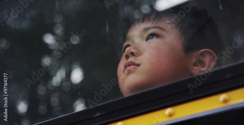 Young asian boy looking out the window of the school bus