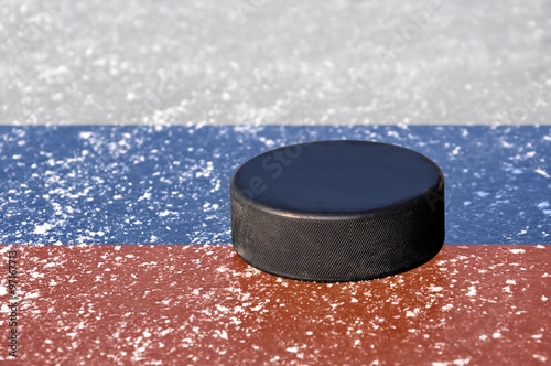 Black hockey puck on ice rink with Russian flag.