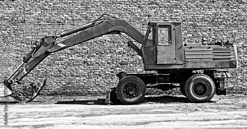 Old red excavator with bucket against the background of a brick wall