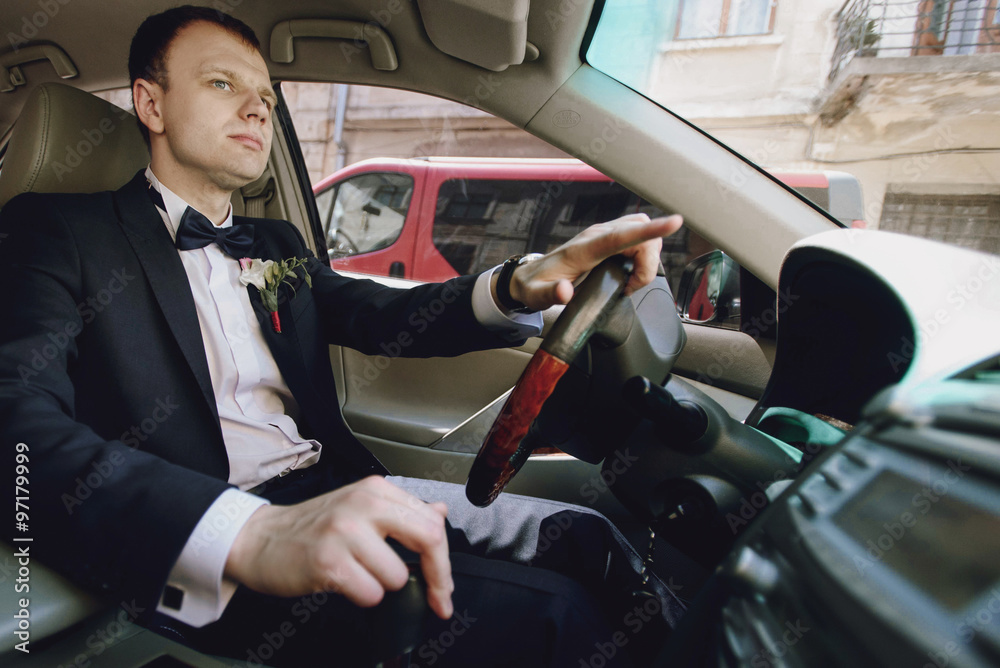 gorgeous elegant stylish groom driving luxury car on the backgro