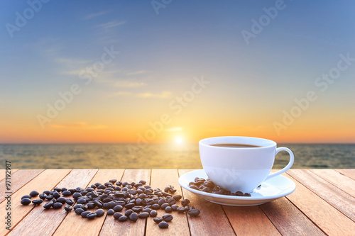 White coffee cup and coffee beans on wood table and view of suns