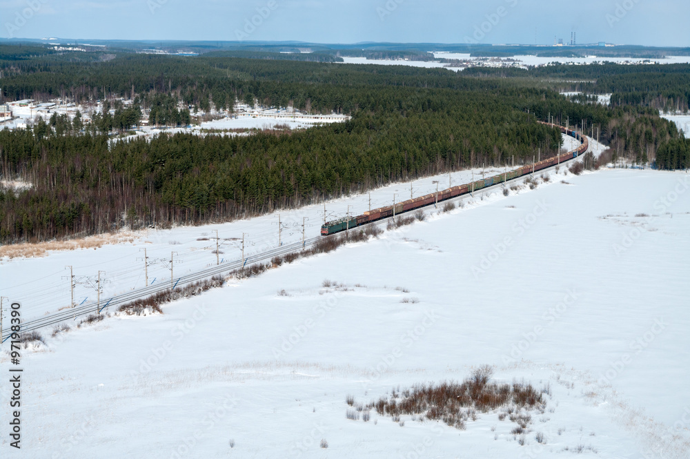 Naklejka premium Freight train driving in snow field in northern winter forests, aerial view
