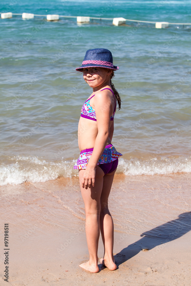 beautiful little girl in bathing suit and cap standing on beach