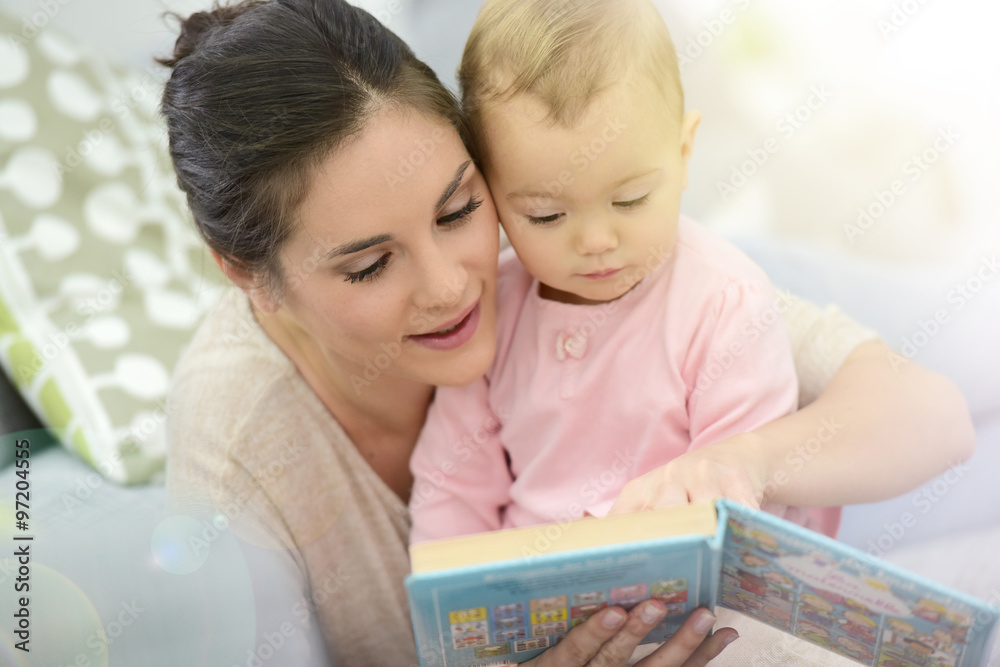 Mother and daughter reading book sitting in sofa Mother and daughter reading book sitting in sofa