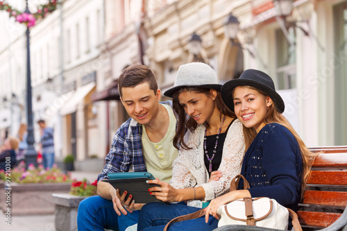 Foto Three friends sit together with tablet on bench