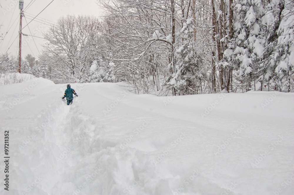 young boy walking down a snow covered rural road in a snow storm