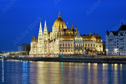Eveninig view of the Hungarian Parliament Building in bright yellow illumination. View from the bank of Danube in Budapest, Hungary.