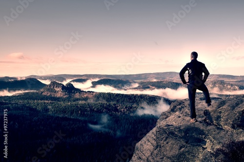 Adult hiker stand on cliff of sandstone empires park and watching over the misty and foggy morning valley