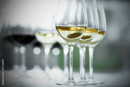 Wineglasses with white and red wine on wooden table on bright background