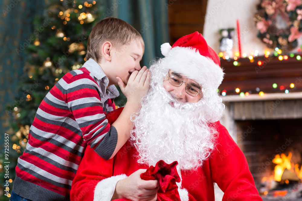 Santa Claus and child boy. Kid telling his Christmas wish in Santa Claus near the Christmas tree opposite fireplace Santa Claus and child boy. Kid telling his Christmas wish in Santa Claus near the Christmas tree opposite fireplace