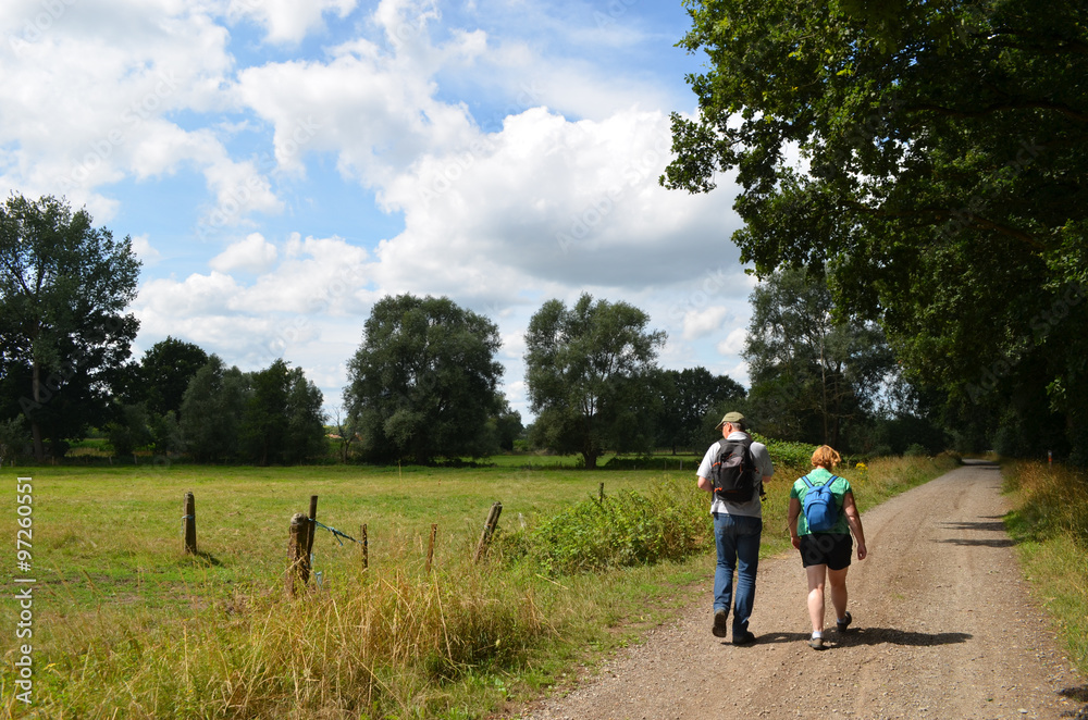 Man and woman hiking on a gravel road next to a meadow Man and woman hiking on a gravel road next to a meadow