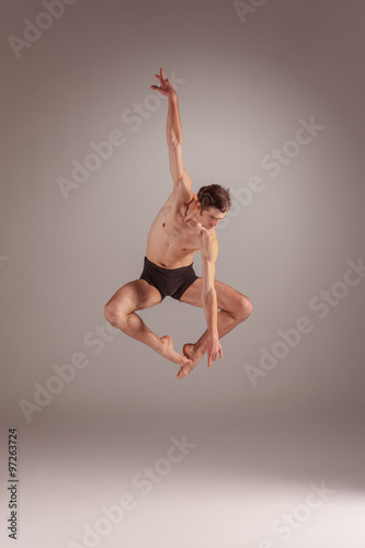 The young attractive modern ballet dancer jumping on gray background