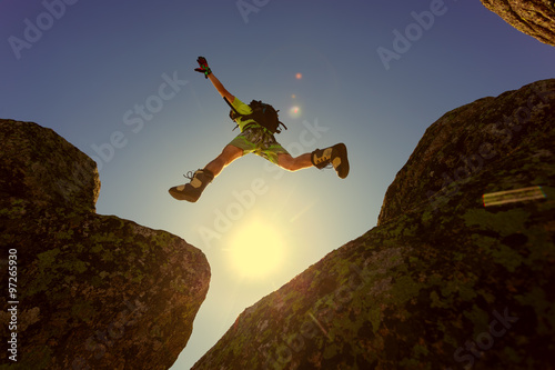 man jumping cliff with blue sky