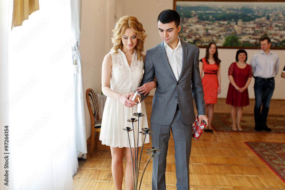 Fototapeta premium stylish beautiful blonde bride with elegant handsome groom lighting candle in registry