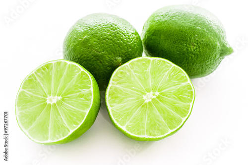 Close up photo of two cut-in-half slices of lime, with two whole limes behind. The background is isolated.