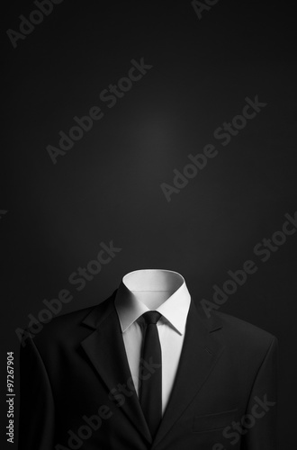 Surrealism and business theme: a man without a head in a black suit on a dark background in the studio photo