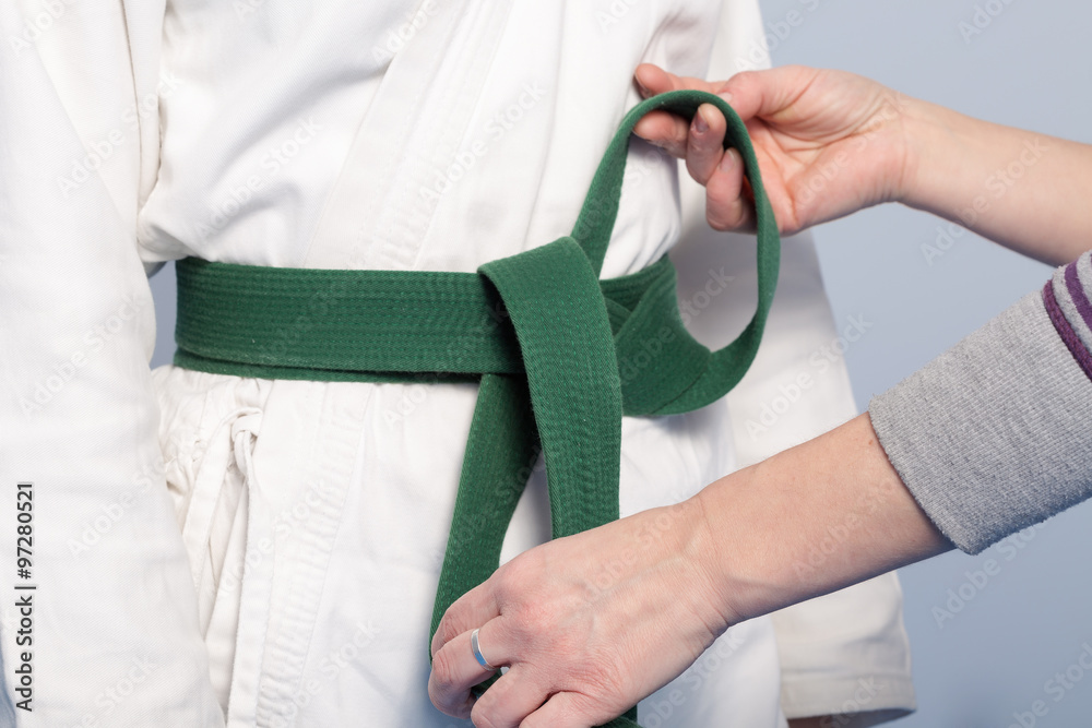 Hands of a parent who helps a child to tie a green belt