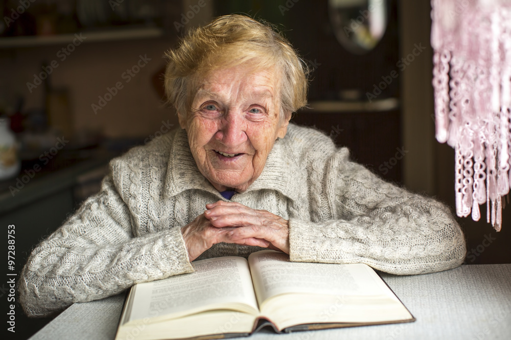 An elderly woman sits with a book at the table.
