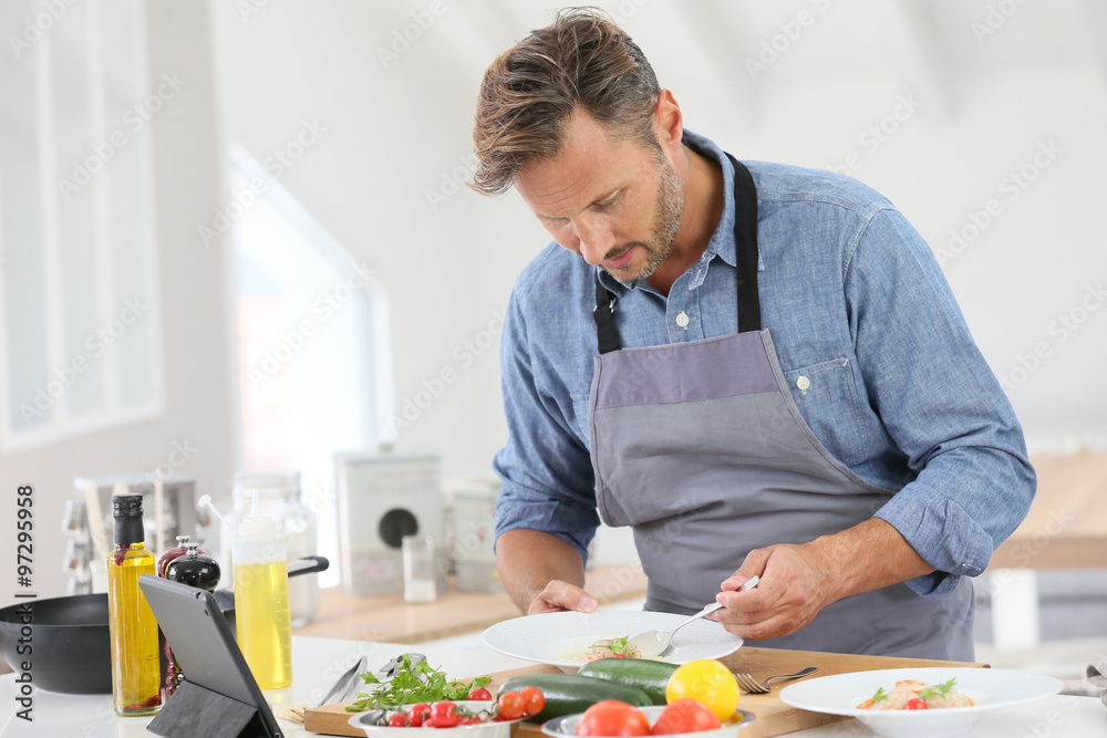 Man in kitchen cooking dish and using digital tablet
