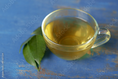 Glass cup of tea with green leaves on blue wooden background