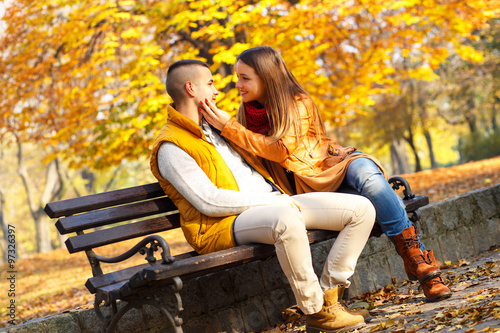 Young couple sitting on a park bench on a sunny autumn day and expressing tenderness