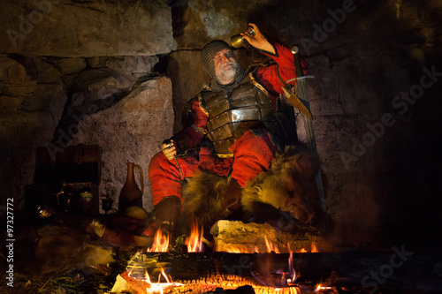 Medieval King in armor is looking at the empty cup of wine