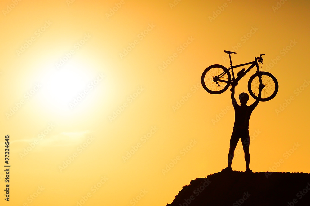 Obraz premium silhouette of a mountain bike cyclist standing on the mountain raising his bike