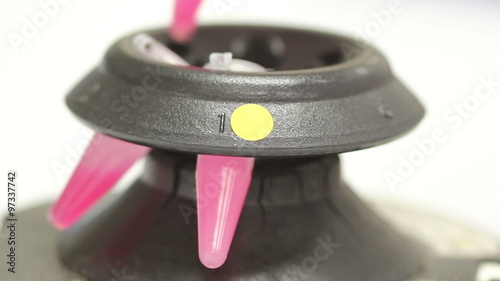 Close up view of an old micro centrifuge with a mixed suspension in eppendorf tubes placed in and being separated into a red organic and clear aqueous phase.