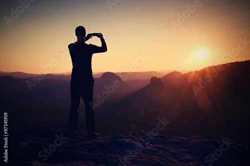 Hiker is taking photo by smart phone on the peak of mountain at sunrise. © rdonar