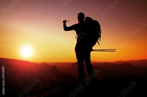 Strong man hiker taking photo with smart phone at mountain peak. Daybreak at horizon