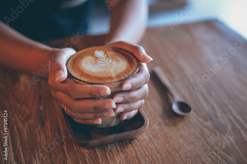Woman hand hold cup of coffee latte on the wood texture   in vintage color tone photo