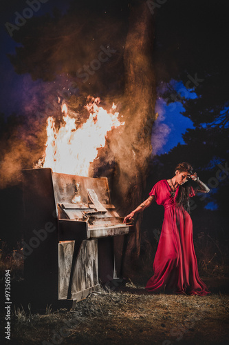 Woman in red dress playing burning piano