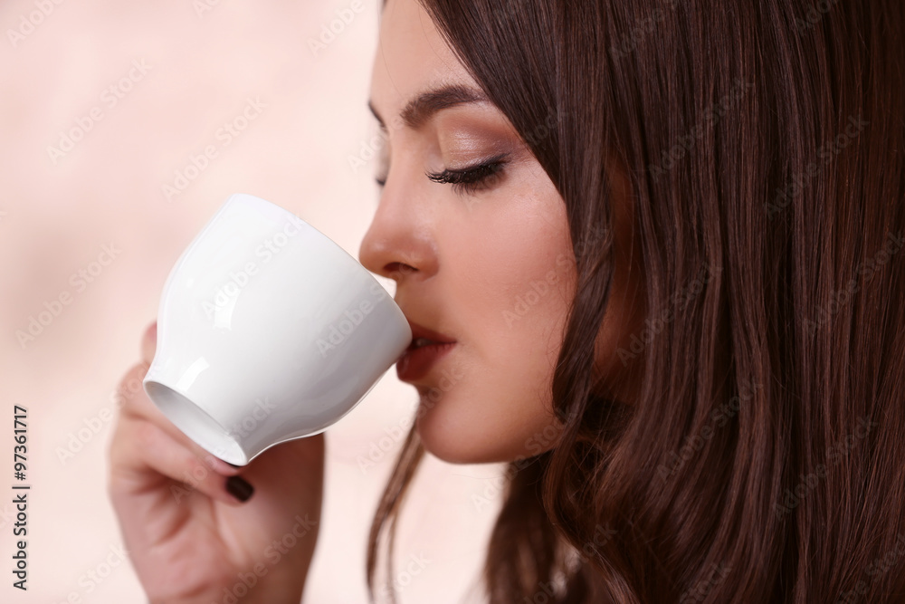 Beautiful young woman drinking coffee on pink blurred background Beautiful young woman drinking coffee on pink blurred background