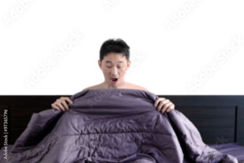 Blurred of surprised naked young man in bed looking down at his photo