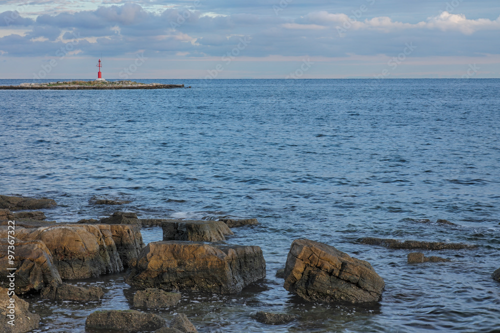 Sea stones at sunrise, on background lighthouse on  island.